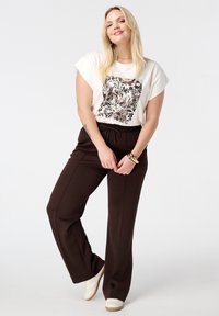 Lichtcrème t-shirt met een donkere bloemenprint, gecombineerd met bruine wijde broek. Soepele stof, ontspannen ontwerp, met een elastische tailleband.