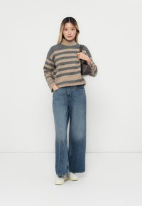 Stripet strikkegenser i grå og beige, sammen med løse blå denimjeans og hvite sneakers. Vesken er mørkegrå og teksturert.