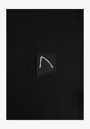 Crna pletena tkanina s kvadratnom označnom etiketom s bijelim apstraktnim linijskim dizajnom. Tekstura izgleda glatko i ujednačeno.