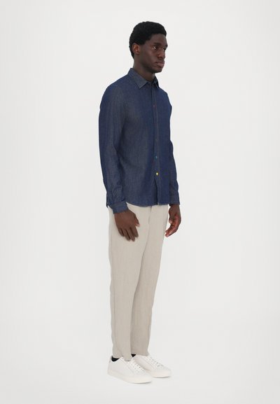 Denim button-up shirt with long sleeves, dark blue, featuring multicolored buttons. Paired with light beige pants and white sneakers.