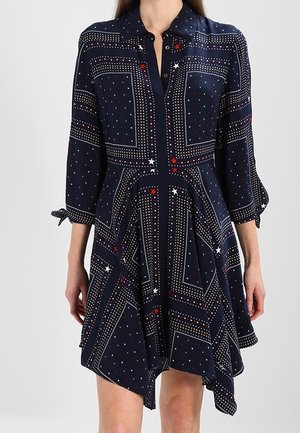 Marineblaues Kleid mit Kragen, dreiviertel Ärmeln und asymmetrischem Saum. Mit weißen, roten und blauen Sternenmustern und gepunkteten Designs.