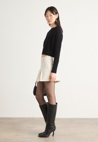 Svart kabelstickad kort jumper, beige plisserad minikjol, genomskinliga svarta strumpbyxor, knähöga svarta läderstövlar, liten svart handväska.