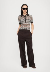 Knitted polo shirt with a wavy pattern in muted colors; paired with black wide-leg pants featuring a zigzag texture and subtle sheen.