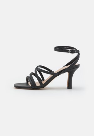 Sort strappy højhælet sandal med flere tynde stropper, ankelspænde, firkantet tå og en slank, buet hæl. Glat tekstur.