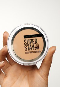 Maybelline Super Stay-foundation i en rund, genomskinlig kompakt. Ljusbrun puderstruktur inuti med svart och silver branding på toppen.