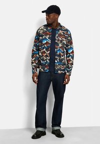 Multicolored camouflage shirt, cotton blend, long sleeves, buttoned front, paired with dark denim jeans and black shoes. Casual cap included.