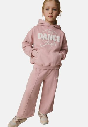 Rosa Fleece-Hoodie mit dem Text "DANCE Studio", kombiniert mit passenden weit geschnittenen Sweatpants. Beide Teile haben gerippte Bündchen und eine weiche Textur.