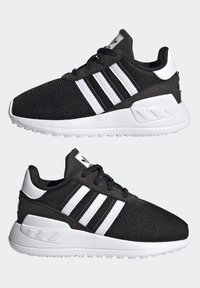 Svarta träningsskor med ovandel i mesh, vit design med tre ränder och gummisula. Har vadderad krage och plös, samt texturerade detaljer.