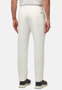 Pantalon blanc ajusté, doté de deux poches arrière et d'une texture lisse. Porté avec des baskets sombres.