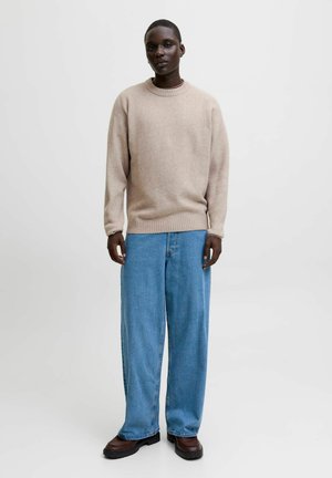 Beige knit sweater with a round neck, paired with loose blue denim pants. Dark shoes complete the outfit, featuring a simple, casual style.