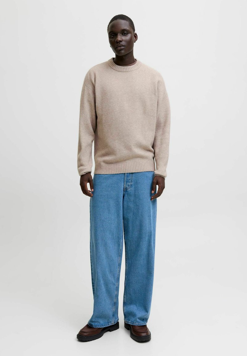 Beige stickad tröja med rund hals, i kombination med lösa blå denimbyxor. Mörka skor kompletterar outfiten, som har en enkel, avslappnad stil.