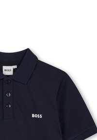 Polo shirt bleu marine en tissu texturé. Il dispose d'une patte de boutonnage à trois boutons, d'un col côtelé et d'un logo "BOSS" blanc sur la poitrine.
