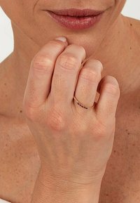 Guldring på ett finger, med små färgade ädelstenar satta i ett linjärt mönster. Slät yta, smal banddesign. Hudton synlig.