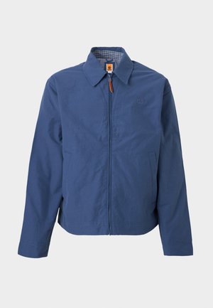 Tmavomodrá bunda na zips s golierom, bočnými vreckami a malým vyrazeným logom na ľavej strane hrudníka, zobrazená na jednoduchom pozadí.