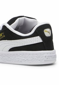Baskets en suede noir avec accents blancs, dotées d'une semelle en caoutchouc blanc texturé et d'un logo Puma doré à l'arrière. Design classique à tige basse.