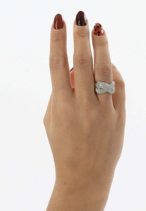 Hand with brown, dark brown, and leopard print nail polish, wearing a silver rhinestone bow-shaped ring on the ring finger.