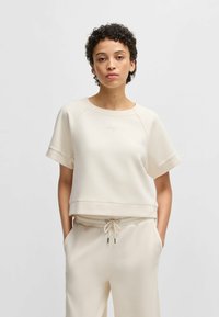 Cream-colored short-sleeve sweatshirt with a relaxed fit, rounded neckline, and subtle embroidered logo; smooth fabric with ribbed hem.