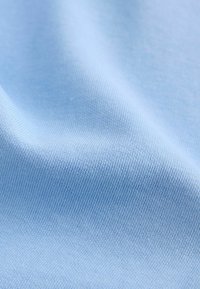 Světle modrá látka s hladkým povrchem, která má jemný žebrovaný vzor. Materiál vypadá pružně a je na dotek měkký.