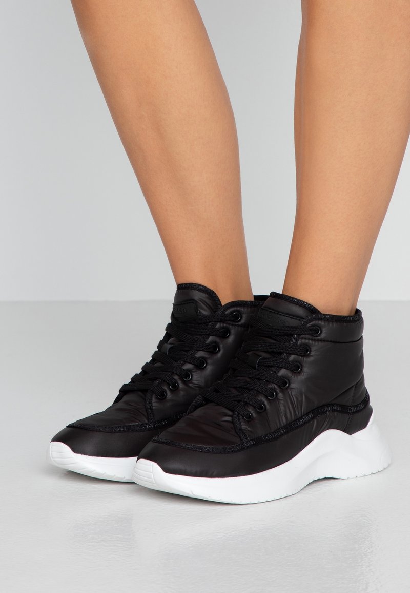 Baskets montantes noires en matière synthétique lisse, dotées d'une semelle blanche, d'un col rembourré et de lacets noirs.