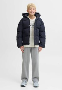 Marineblå pufferjakke med lynlås foran og hætte, parret med en let t-shirt og grå sweats. Har polstrede sektioner og elastiske manchetter.