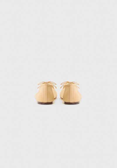 Yellow canvas ballet flats with light brown leather accents and ties at the back, rounded toe, and a low-profile sole.