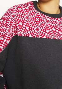 Sudadera gris con un patrón floral en rojo y blanco en los hombros, con un cuello redondo y una textura suave.
