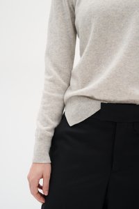 Light gray sweater made of soft fabric with ribbed cuffs, paired with black high-waisted trousers featuring a flat front and structured waistband.