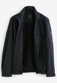 Zwarte lichtgewicht jas met ritssluiting aan de voorkant, opstaande kraag en meerdere zakken. Gladde textuur met een mesh voering en een merkembleem aan de binnenkant.