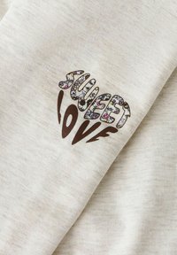 Sudadera de color crema con el texto "SWEET LOVE" en patrones florales y acentos marrones, con un acabado suave y texturizado.