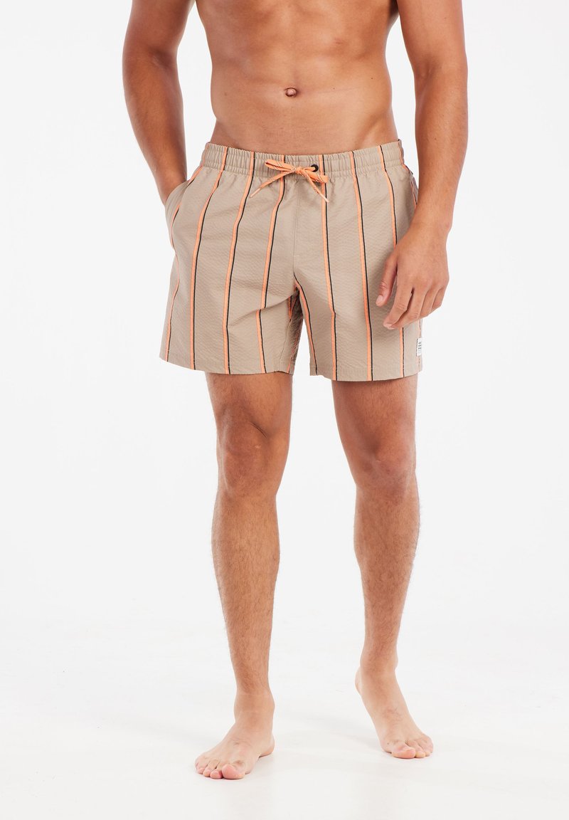 Shorts beige avec des rayures verticales orange et noires, taille élastique et cordon de serrage. Tissu texturé avec poches latérales.