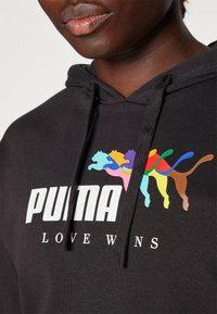 Felpa nera con cappuccio e logo "PUMA" bianco, accompagnata da un grafico color arcobaleno di gatti stilizzati. Presenta un cappuccio regolabile e una texture morbida.