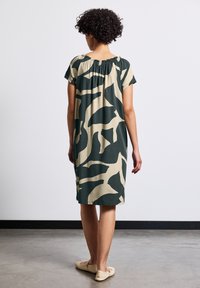 Kortärmad klänning i mörkgrön och krämfärgad abstrakt mönster, med en draperad halsringning och en avslappnad passform, med knälång nederdel.