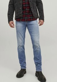 Jean en denim bleu clair à effet délavé, coupe slim, porté avec une veste noire et une chemise en flanelle à carreaux, associé à des bottines noires.