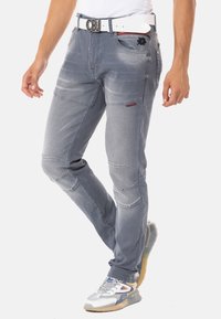 Graue Jeanshosen mit Kniepaneelen, kontrastierenden Nähten und einem weißen Gürtel mit Metallschließe. Ausgestattet mit Taschen auf beiden Seiten.