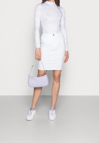 Lichtpaarse lange mouwen top met wolkenpatronen, witte denim rok, lavendel mini handtas en witte sneakers met paarse accenten.