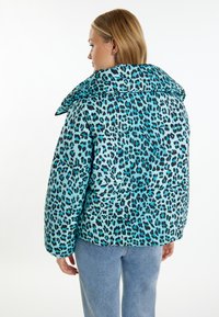 Zateplená bunda v světle modré barvě s černým leopardím vzorem. Má široký límec a spadlé ramena. Měkká textura s viditelnými stehovými detaily.