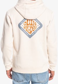 Krémová mikina s kapucí na tkaničku, na zadní straně s diamantovým oranžovo-modrým grafickým logem. Měkká textilie.