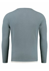 Maglietta a maniche lunghe di colore azzurro chiaro realizzata in materiale a costine. Presenta un collo rotondo e un orlo bianco nella parte inferiore. Dettagli di superficie texture.
