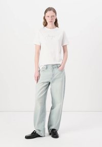 Tricou alb cu maneci scurte, cu un design imprimat de culoare albastră deschisă, asortat cu blugi evazați de culoare albastră deschisă și pantofi negri. Un ansamblu simplu și casual.