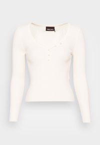 Vit ribbad långärmad topp med rundad halsringning och fyra pärlknappar längs mittfram, figurnära passform.