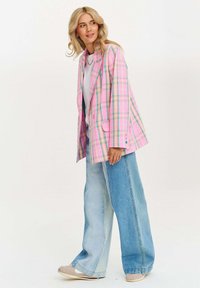 Ružový károvaný blejzer s modrými a žltými akcentmi, s vycibreným strihom a dvoma prednými vreckami, skombinovaný s širokými svetlomodrými džínami.