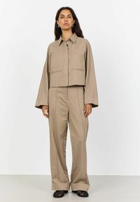 Beige Cropped-Jacke mit zwei Fronttaschen, kombiniert mit einer Hose mit weiter Beinform, die eine Mittelnaht und umgeschlagene Säume hat. Texturiertes Material.