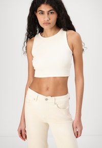 Licht crèmekleurig geribbeld crop top met een ronde halslijn en mouwloos ontwerp, gecombineerd met bijpassende licht crèmekleurige jeans met voorzakken.