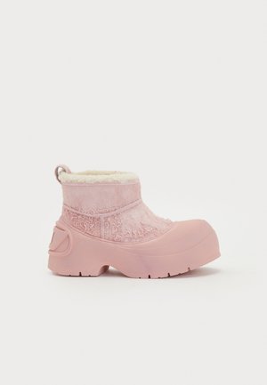 Rosa vattentät ankelsko med en texturerad ovandel och mjukt foder av päls. Funktioner inkluderar en tjock gummisula och en ögla baktill för att dra på skorna.