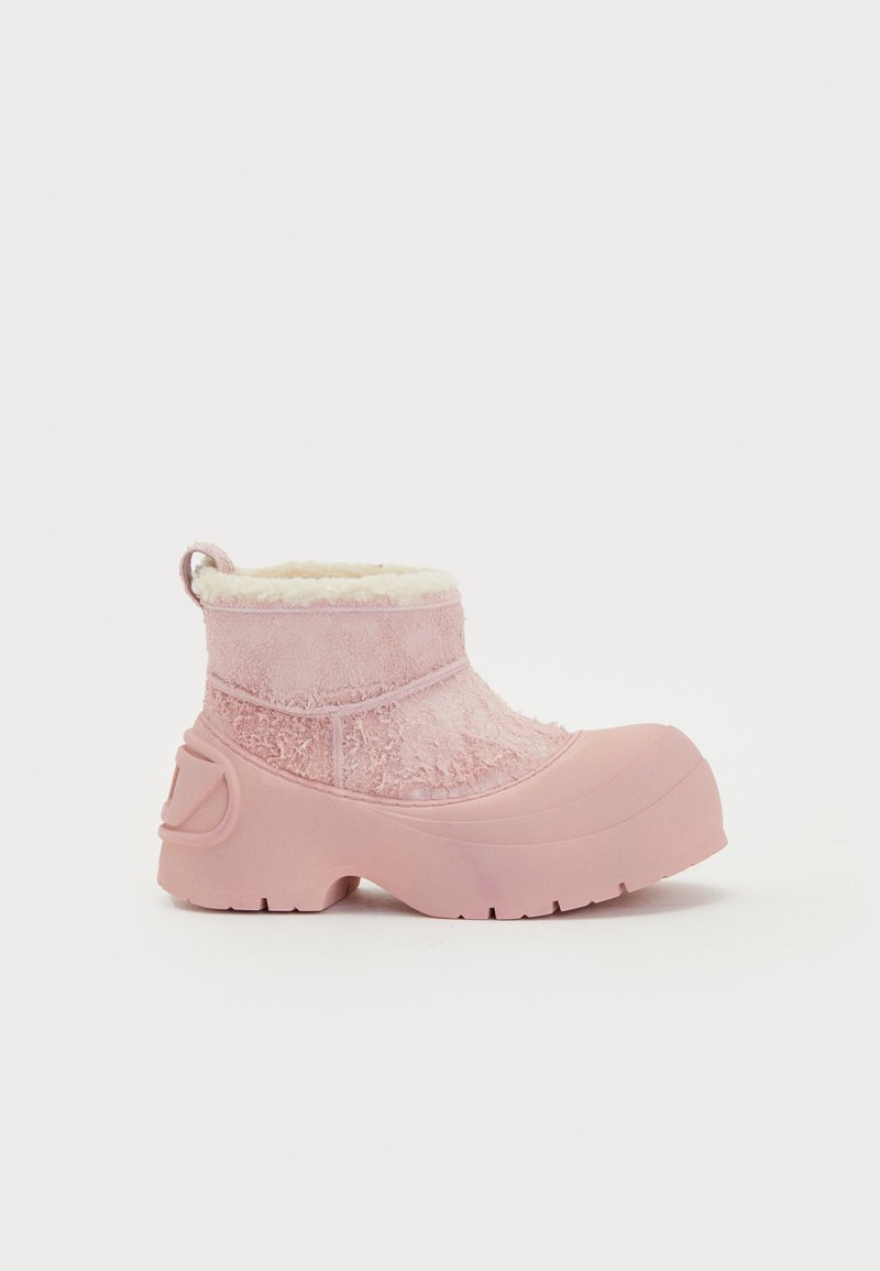 Boots de gleznă impermeabile roz, cu un strat texturat și căptușeală din blăniță moale. Dispune de o talpă groasă din cauciuc și o buclă de prindere în partea din spate.