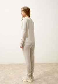 Maglione grigio chiaro a maglia con colletto rotondo, abbinato a pantaloni della tuta grigio chiaro coordinati. Texture morbida e polsini elastici, completati da sneaker beige.