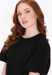 Bluza neagră cu mâneci bufante, confecționată dintr-un material moale, având un decolteu rotund și detalii pliate la umeri. Textură netedă, design simplu.