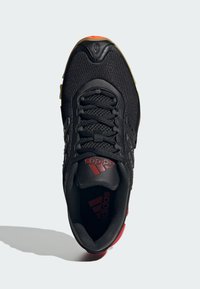 Crne atletske cipele s mrežastim i sintetičkim materijalima, s crvenim naglascima i logotipom. Heksagonalni uzorak na potplatu.