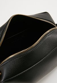 Černá kožená taška na zip se zlatým zipem. Interiér je hladký a nevyložený, obsahuje slot na karty. Pevná konstrukce, kompaktní design.