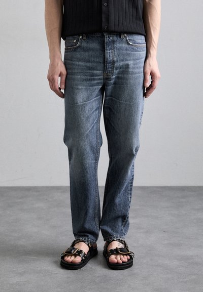 Light blue denim jeans with a relaxed fit, featuring subtle fading and a classic five-pocket design, paired with black sandals and buckles.